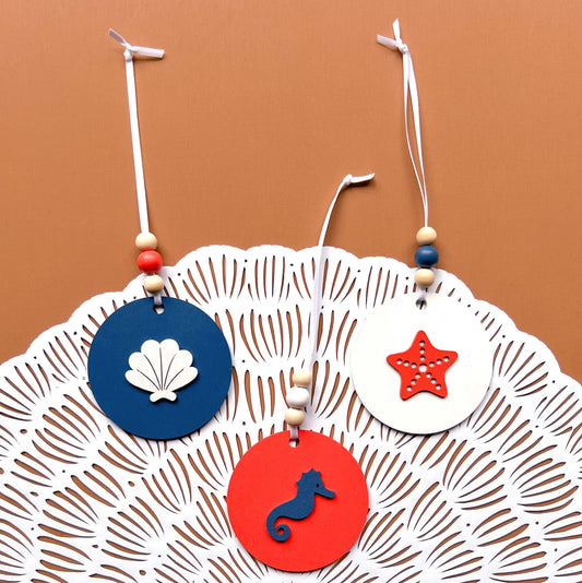 At the Seashore Beachy Set. Three wood ornaments featuring a shell, a seahorse, or a starfish. Summer decor, year-round holiday tree ornament, or gift.