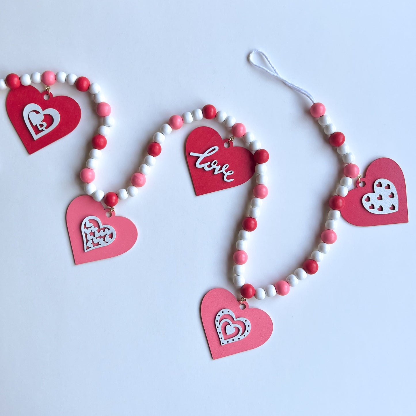Be My Valentine Handmade Garland. Features red or pink wood hearts with smaller hearts or love text. Shapes hang from wood beads. Valentine's day decor or gfit.