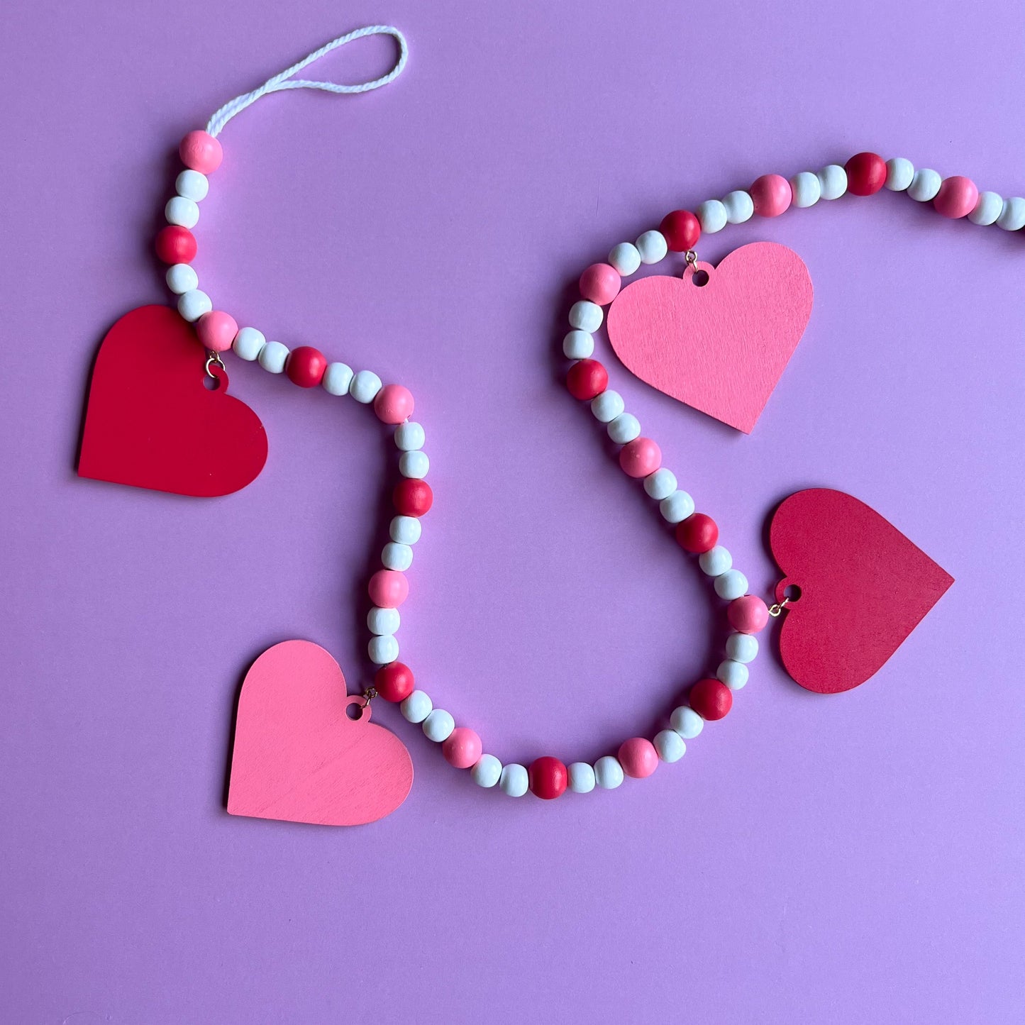 Be My Valentine Handmade Garland. Features red or pink wood hearts with smaller hearts or love text. Shapes hang from wood beads. Valentine's day decor or gfit.