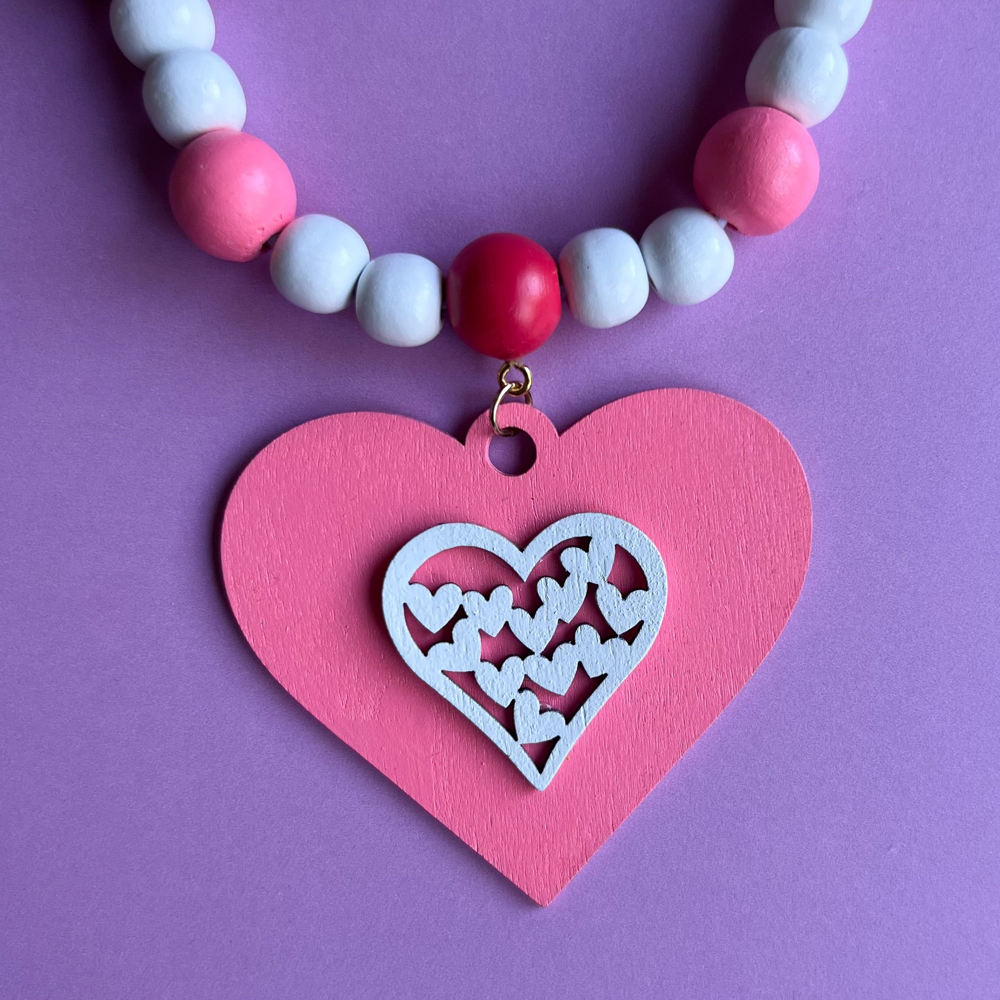 Be My Valentine Handmade Garland. Features red or pink wood hearts with smaller hearts or love text. Shapes hang from wood beads. Valentine's day decor or gfit.