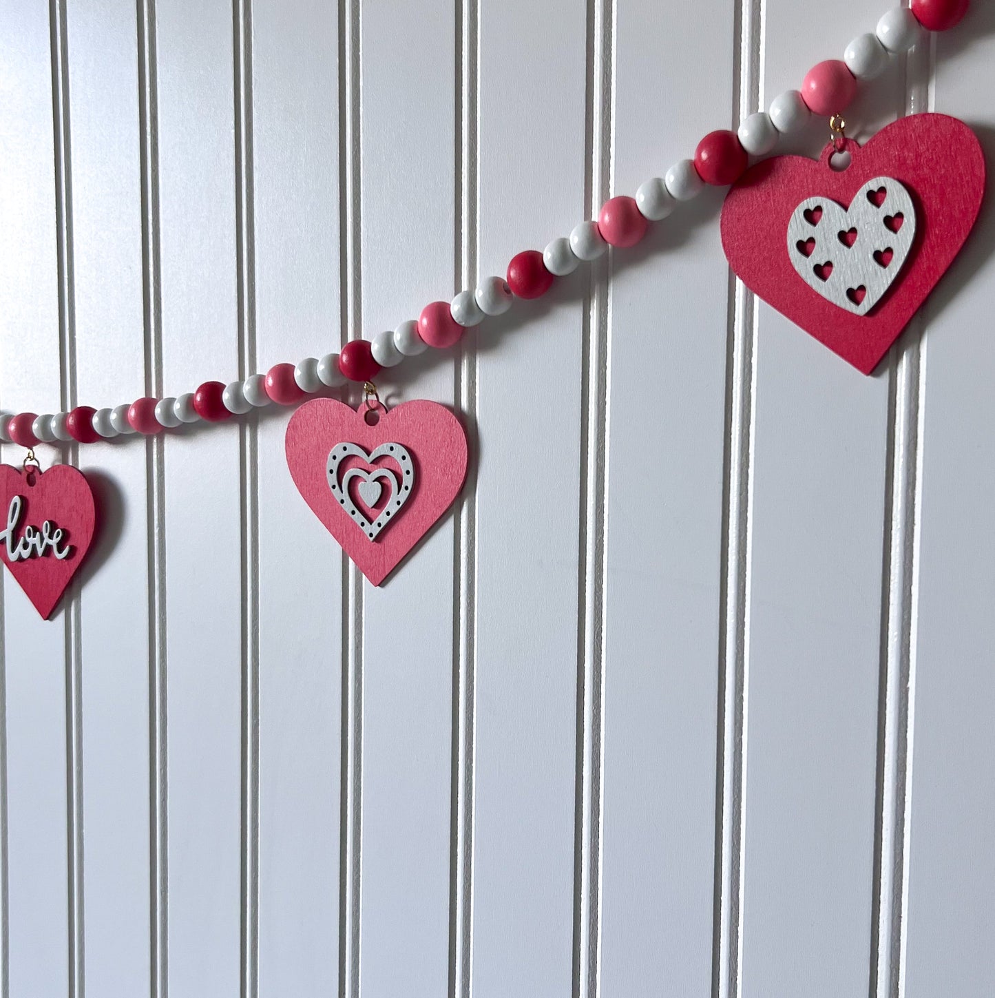 Be My Valentine Handmade Garland. Features red or pink wood hearts with smaller hearts or love text. Shapes hang from wood beads. Valentine's day decor or gfit.