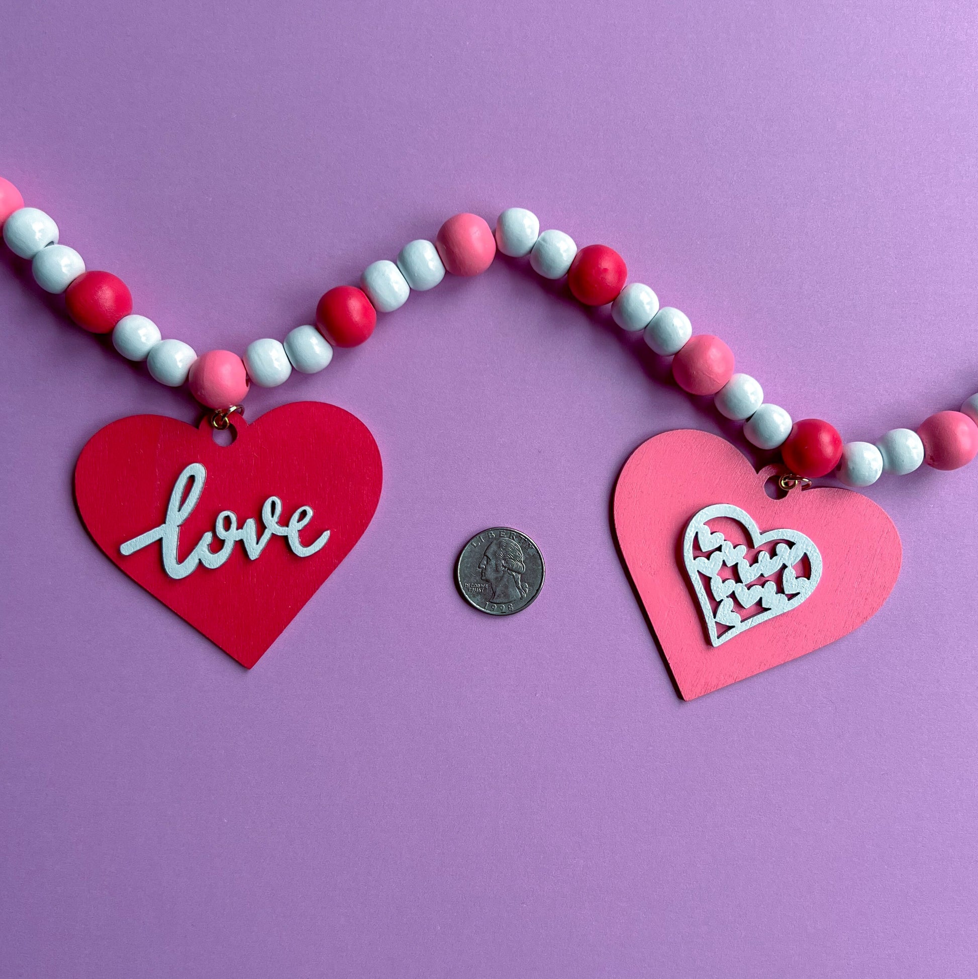 Be My Valentine Handmade Garland. Features red or pink wood hearts with smaller hearts or love text. Shapes hang from wood beads. Valentine's day decor or gfit.