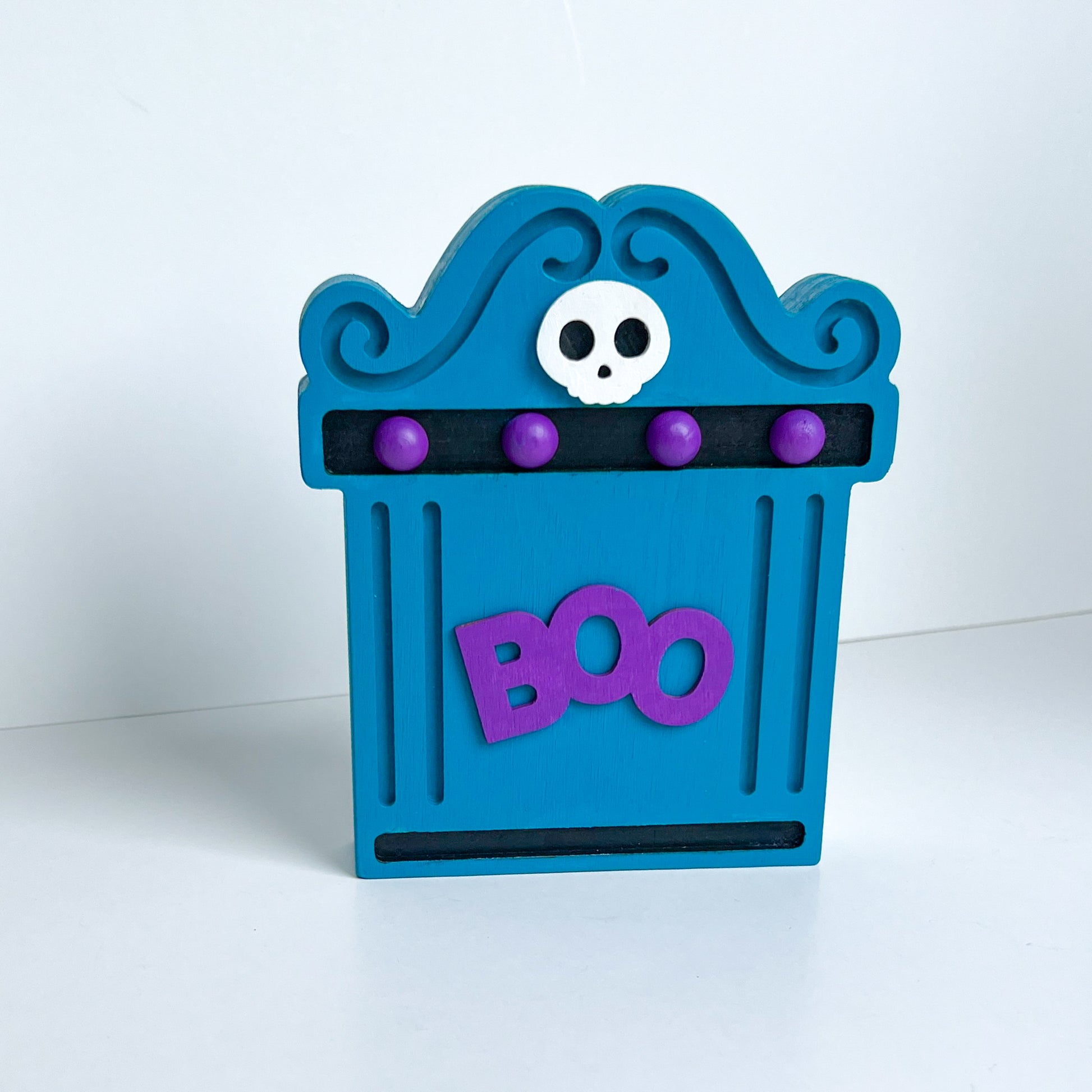 Bright Boo Tombstone Shelf Sitter. Features vibrant colors of blue and purple with a ‘boo’ wood cutout and a little skull. It's free standing, but has a keyhole cutout on the back so can hang on the wall. Halloween decor.