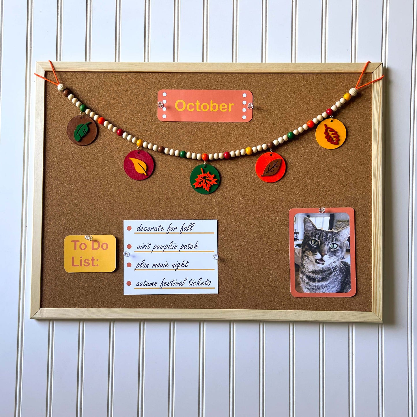 Image shows a wood bead garland with 2" wood circles that feature various colored fall leaves. Circles hang from painted beads with natural wood beads are interspersed. Beads are strung on 2mm orange macrame cord with 3" loops on each end.