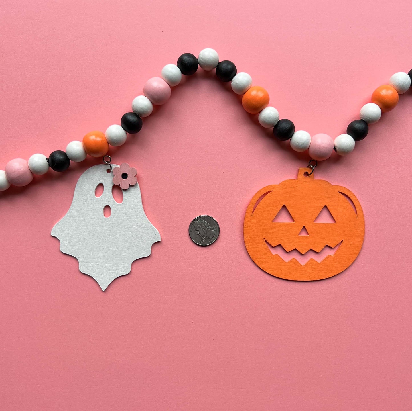 Halloween themed wood bead garland with three ghosts and two pumpkins hanging from beads. Black, white, light orange, pale pink beads and ghosts and pumpkins.