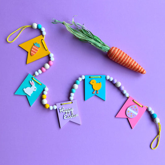 Image shows handmade garland with wood pennants featuring Easter shapes - a carrot, a bunny, a chick, an egg, and a "Happy Easter" wood cutout. Pennants are strung with natural and painted beads; includes 3-inch loops on either end.