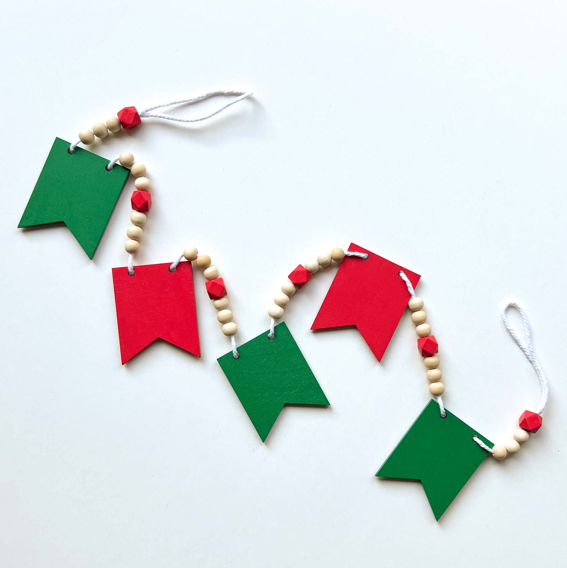 Christmas themed wood bead garland with five wood pennants featuring Christmas themed shapes in red, green, white, and yellow.
