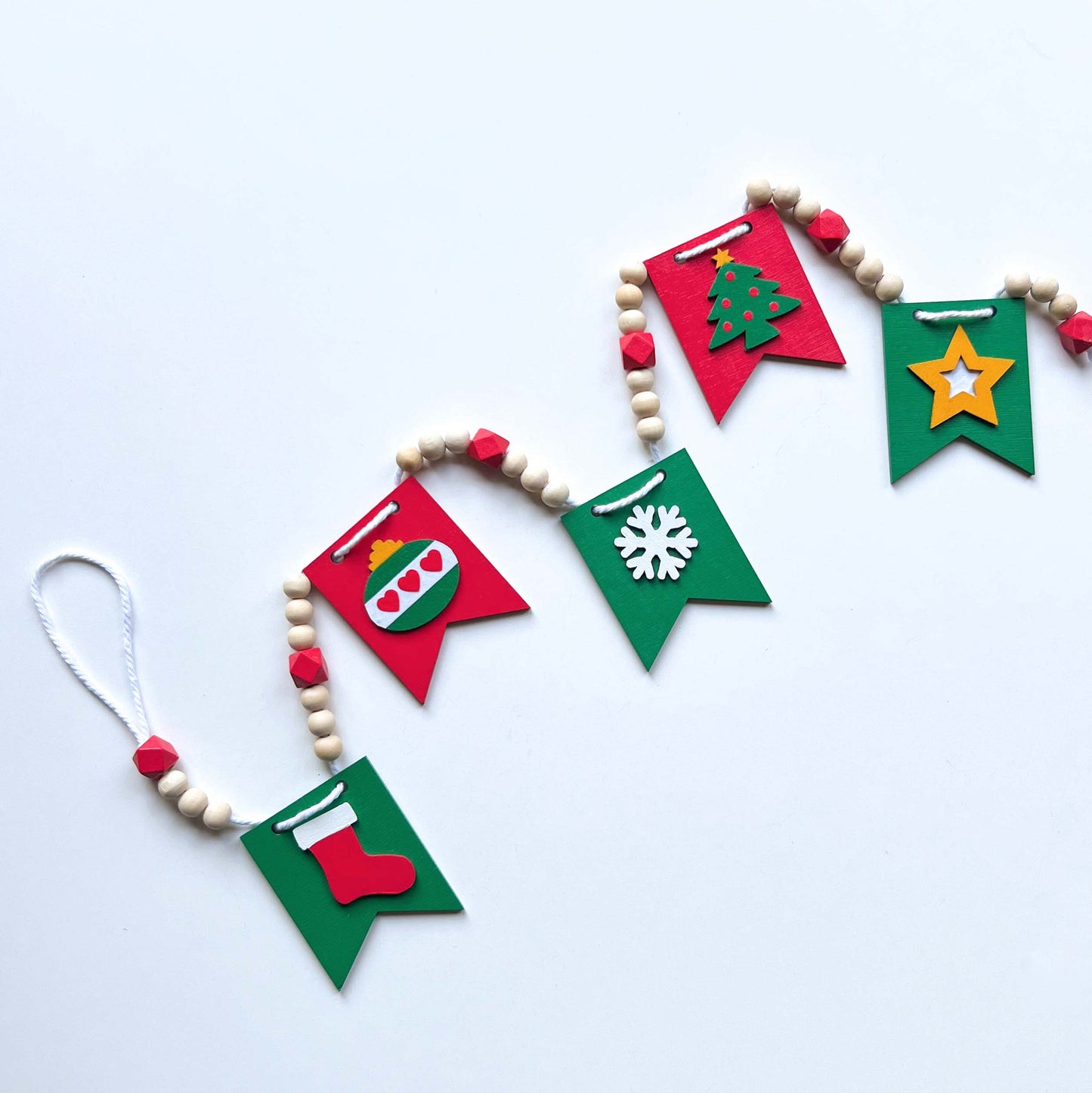 Christmas themed wood bead garland with five wood pennants featuring Christmas themed shapes in red, green, white, and yellow.