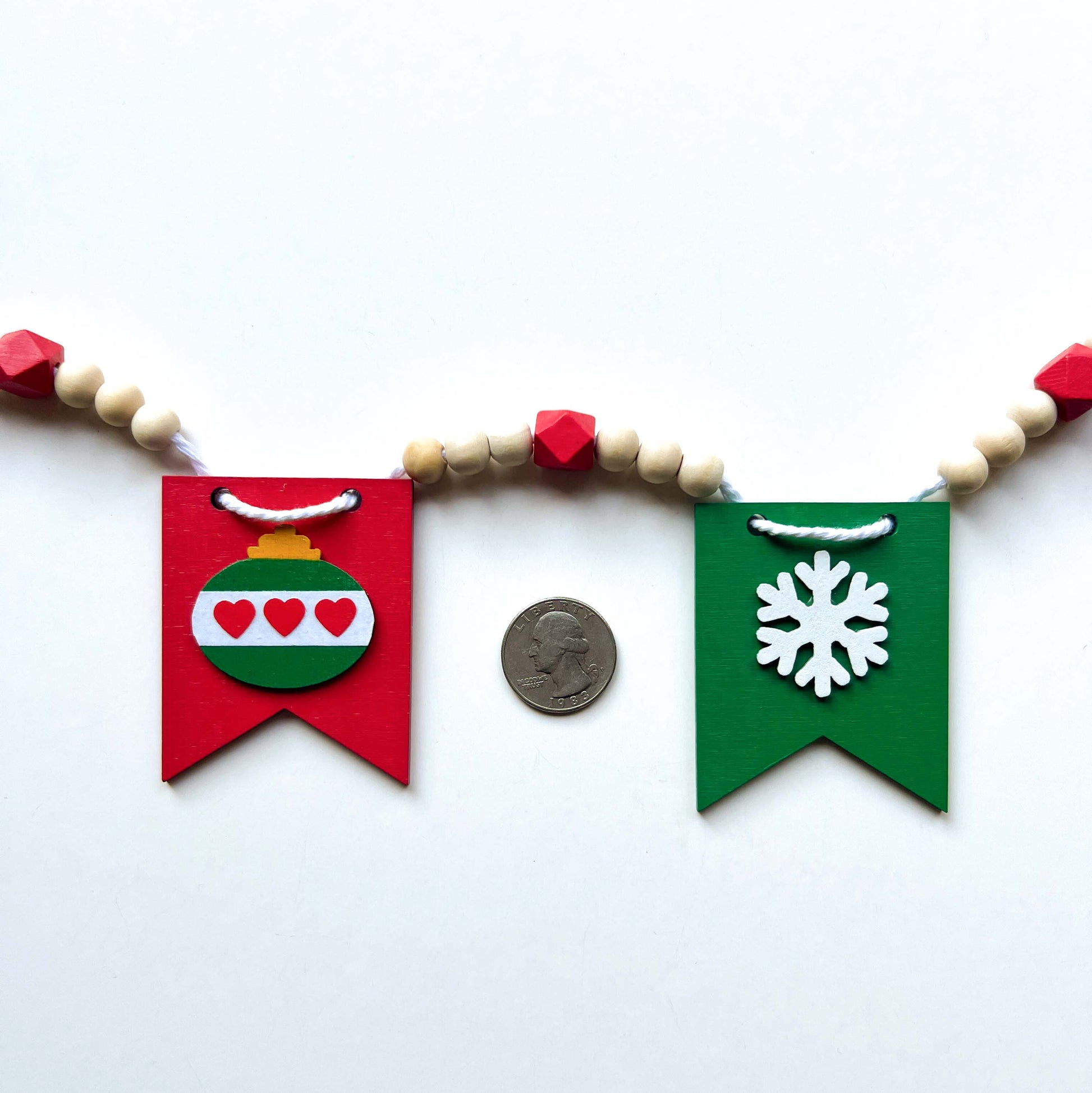 Christmas themed wood bead garland with five wood pennants featuring Christmas themed shapes in red, green, white, and yellow.