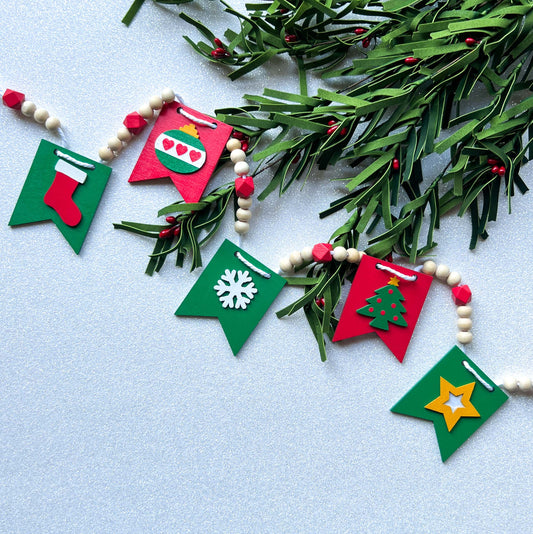 Christmas themed wood bead garland with five wood pennants featuring Christmas themed shapes in red, green, white, and yellow.