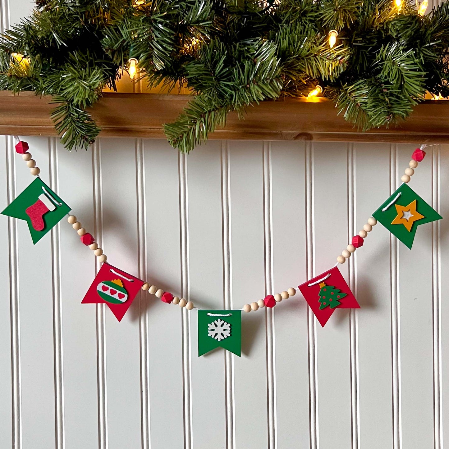 Christmas themed wood bead garland with five wood pennants featuring Christmas themed shapes in red, green, white, and yellow.