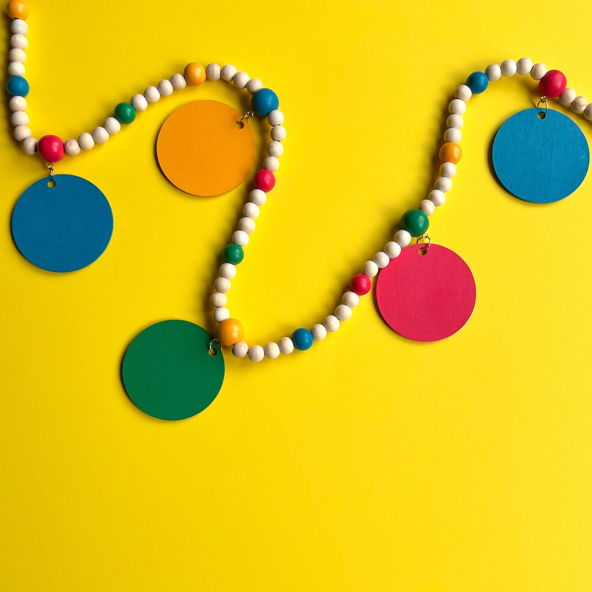 In the Garden Handmade Garland. The garland features wood circles a garden themed shape – a watering can, flower, birdhouse, bluebird, or butterfly. Shapes hang from wood beads. Spring or summer garden seasonal decoration or gift.