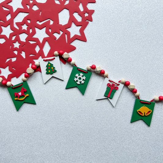 Christmas themed mini garland with pennants featuring Christmas items such as a tree, snowflake, gift, bells, and a rocking horse strung with natural and red beads.