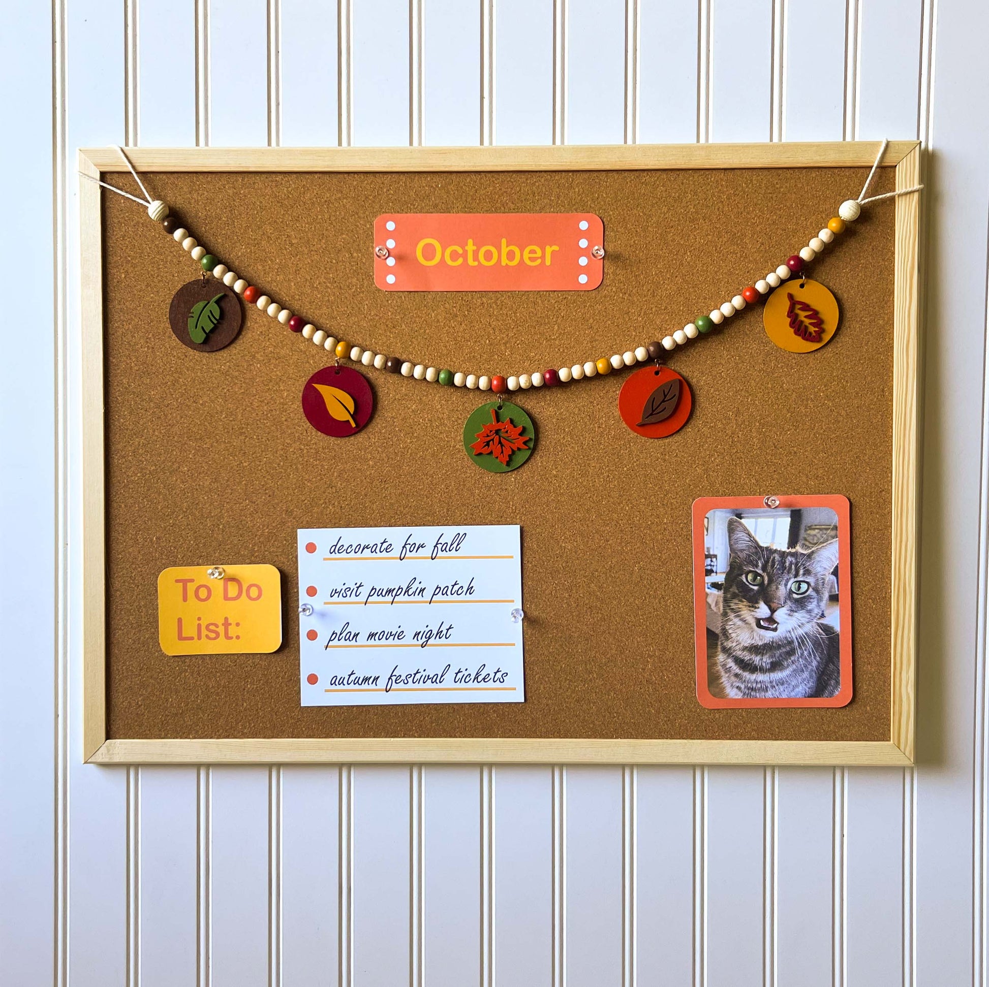 Image shows a wood bead garland with 2" wood circles that feature various colored fall leaves. Circles hang from painted beads with natural wood beads interspersed. Beads are strung on 2mm orange macrame cord with 3" loops on each end.