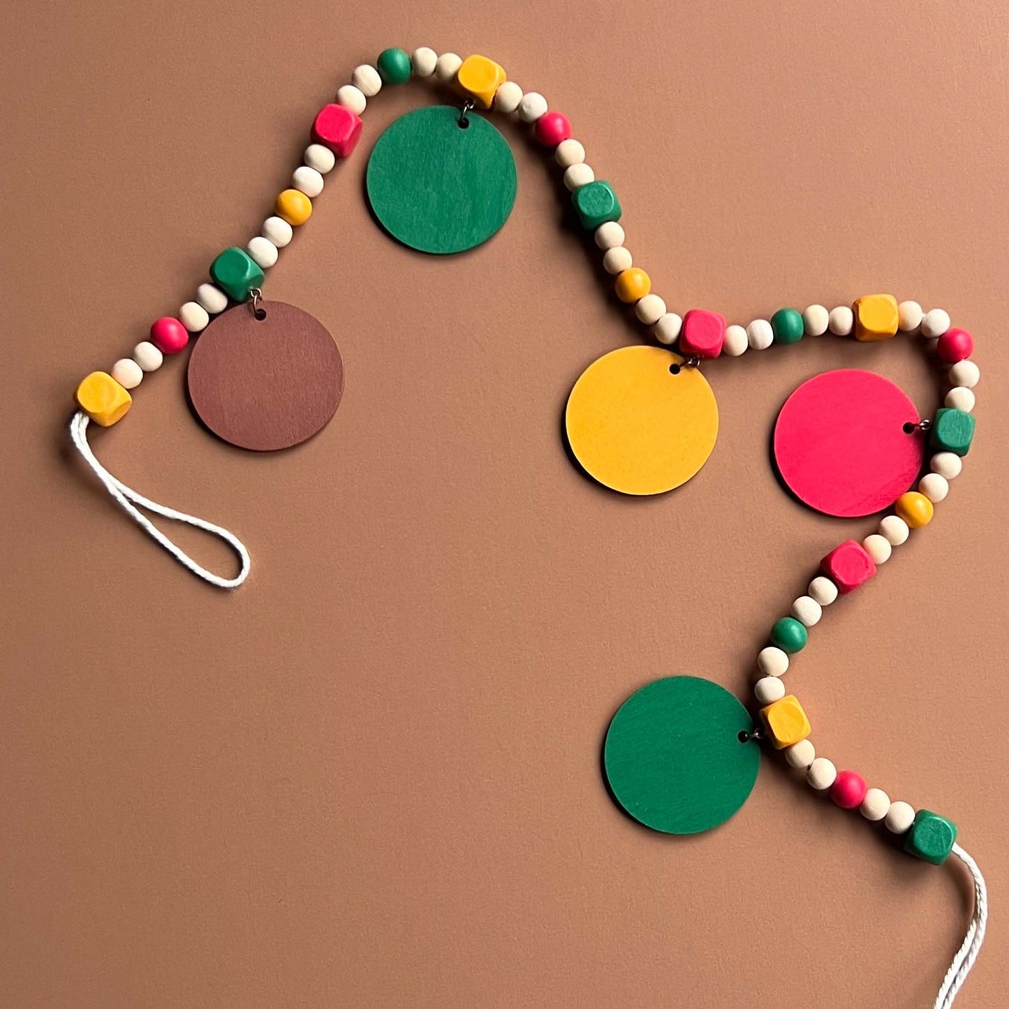Image shows handmade garland with wood circles featuring nature themed shapes. Wood circles hang from painted square beads and are strung with other painted and natural round wood beads. Includes 3-inch loops on either end.