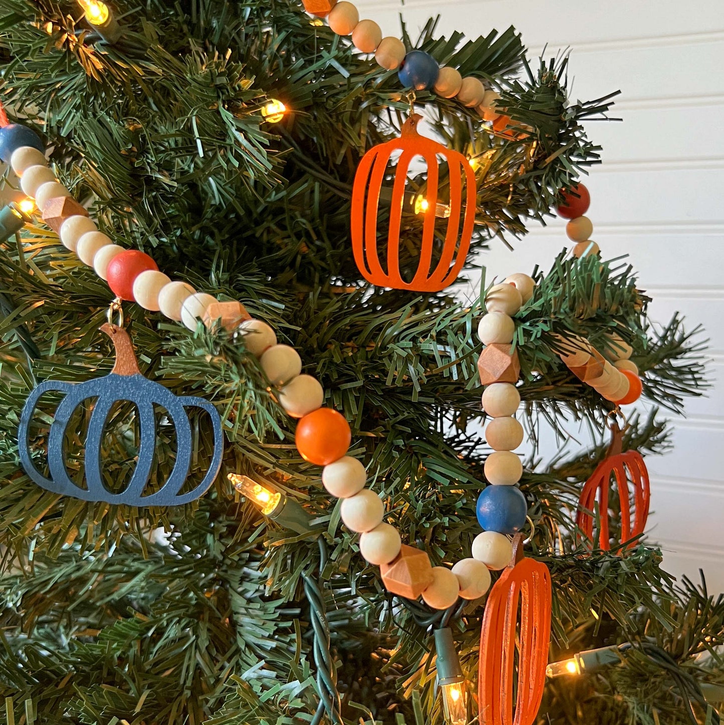 Pumpkin Harvest Handmade Garland. The garland features five wood pumpkins in bright fall colors of orange, rust, and deep blue. Pumpkins hang from painted wood beads. Autumn Thanksgiving seasonal decoration or gift.