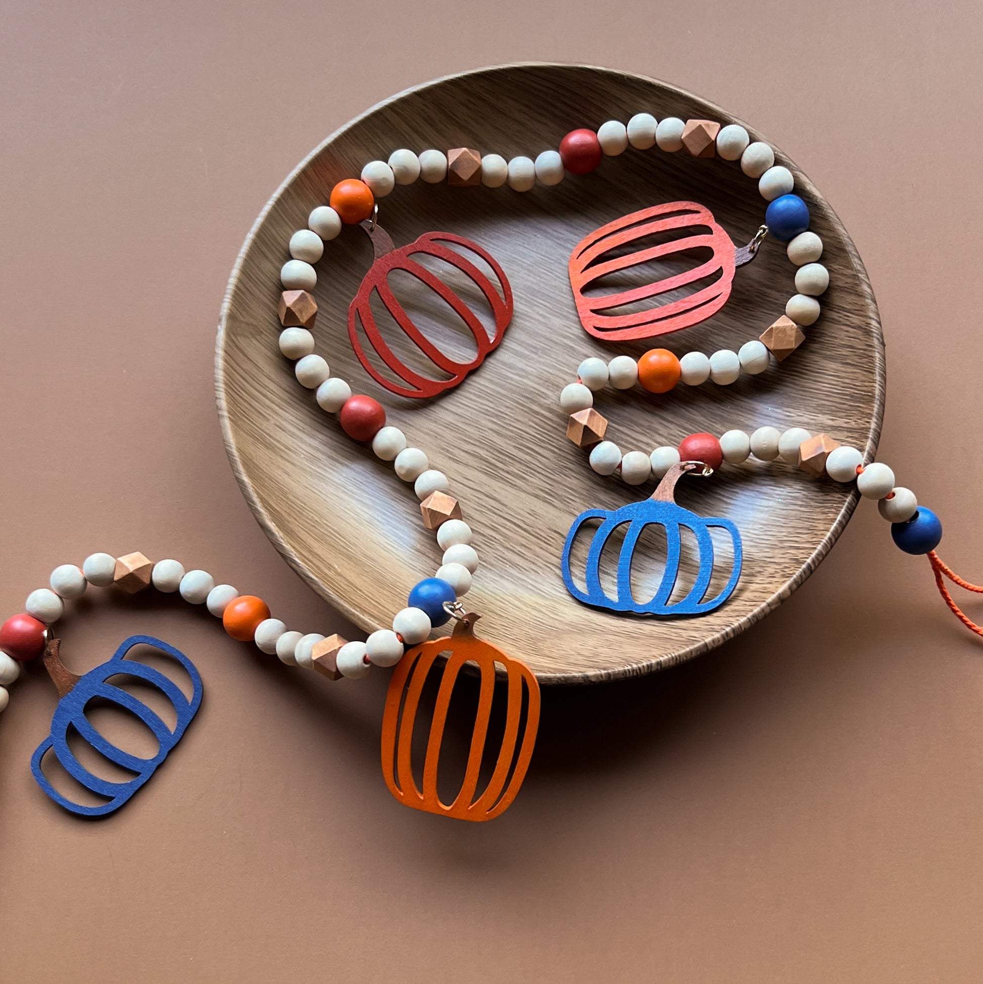 Pumpkin Harvest Handmade Garland. The garland features five wood pumpkins in bright fall colors of orange, rust, and deep blue. Pumpkins hang from painted wood beads. Autumn Thanksgiving seasonal decoration or gift.