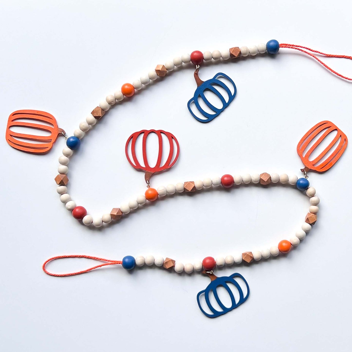 Pumpkin Harvest Handmade Garland. The garland features five wood pumpkins in bright fall colors of orange, rust, and deep blue. Pumpkins hang from painted wood beads. Autumn Thanksgiving seasonal decoration or gift.