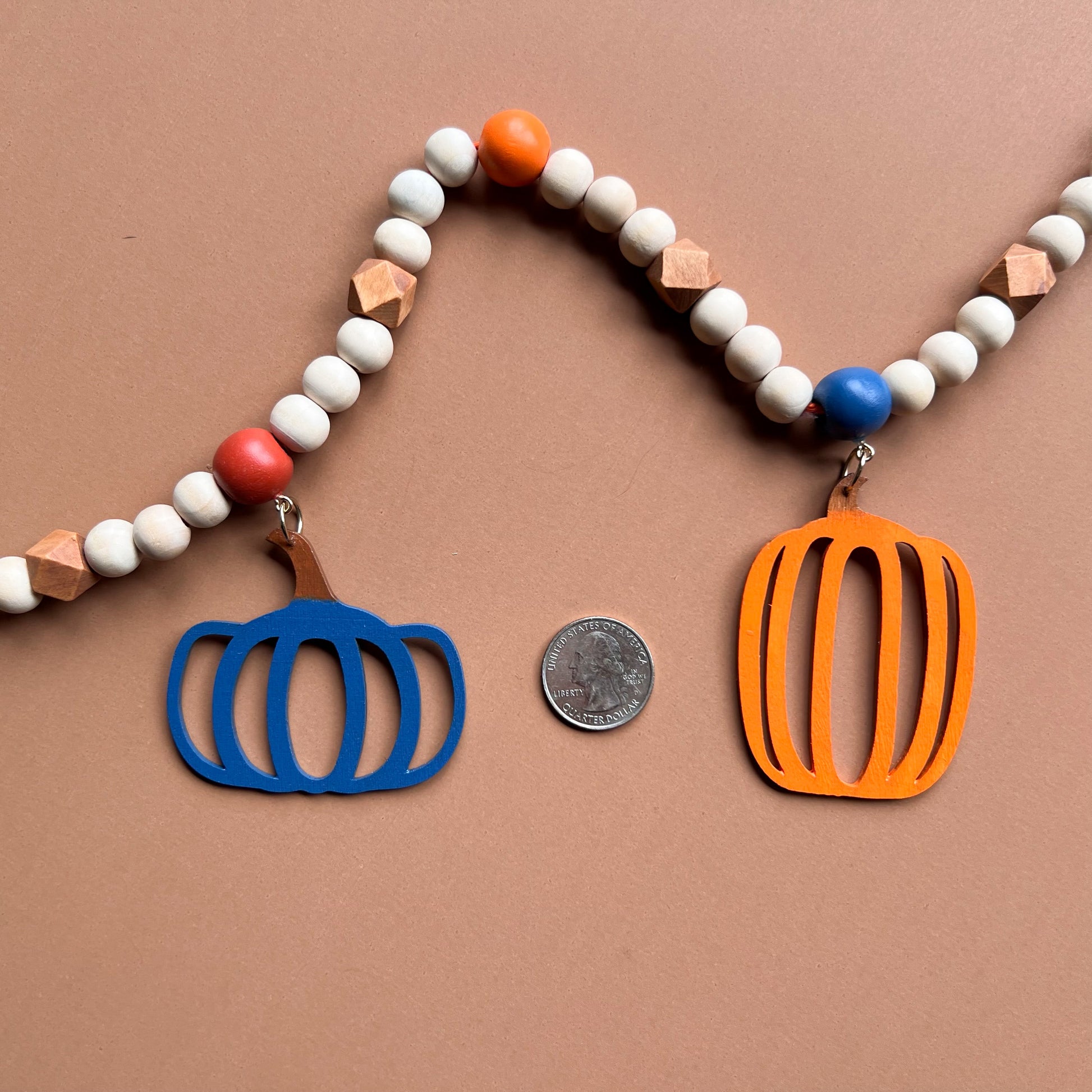 Pumpkin Harvest Handmade Garland. The garland features five wood pumpkins in bright fall colors of orange, rust, and deep blue. Pumpkins hang from painted wood beads. Autumn Thanksgiving seasonal decoration or gift.