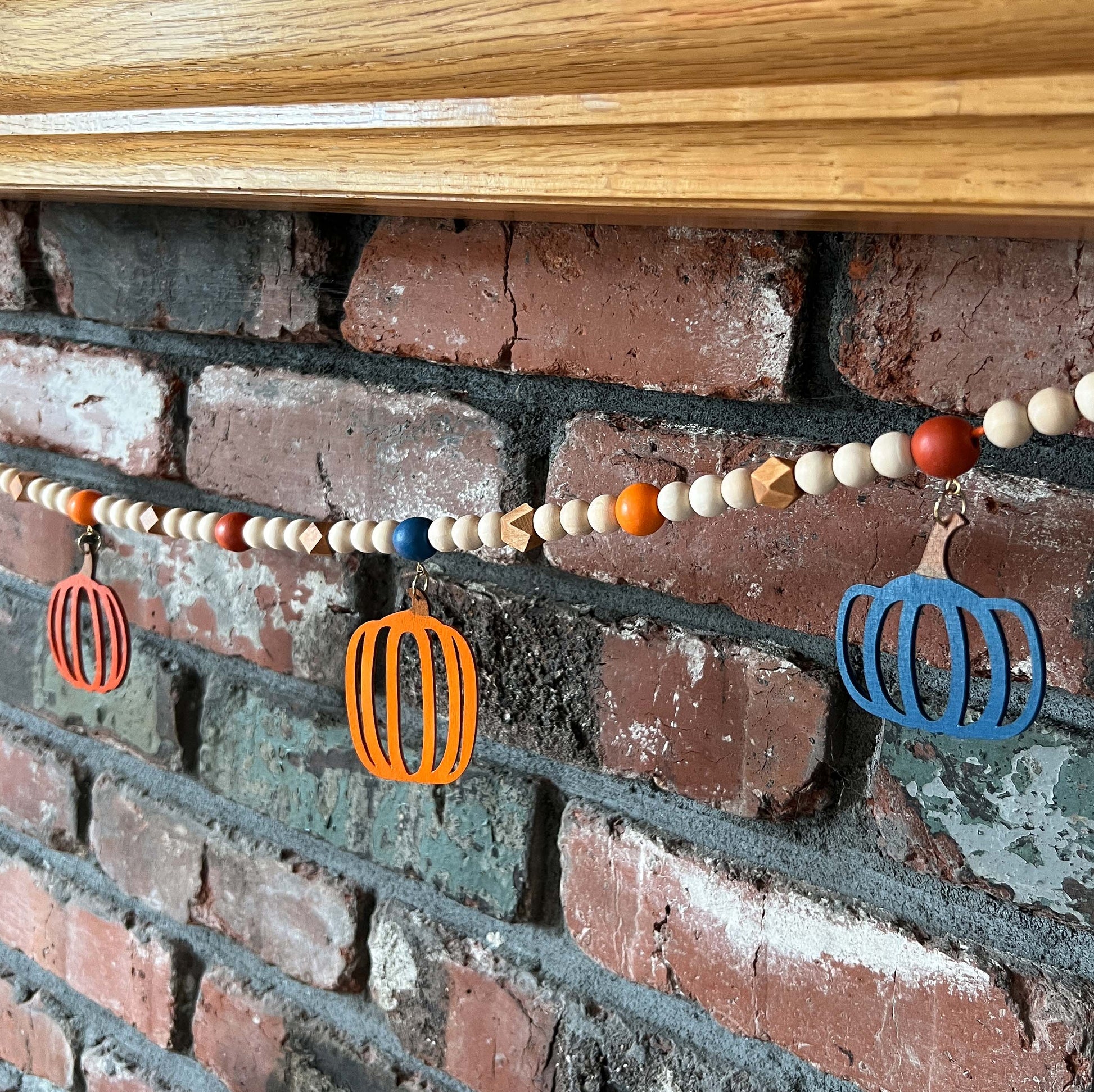 Pumpkin Harvest Handmade Garland. The garland features five wood pumpkins in bright fall colors of orange, rust, and deep blue. Pumpkins hang from painted wood beads. Autumn Thanksgiving seasonal decoration or gift.