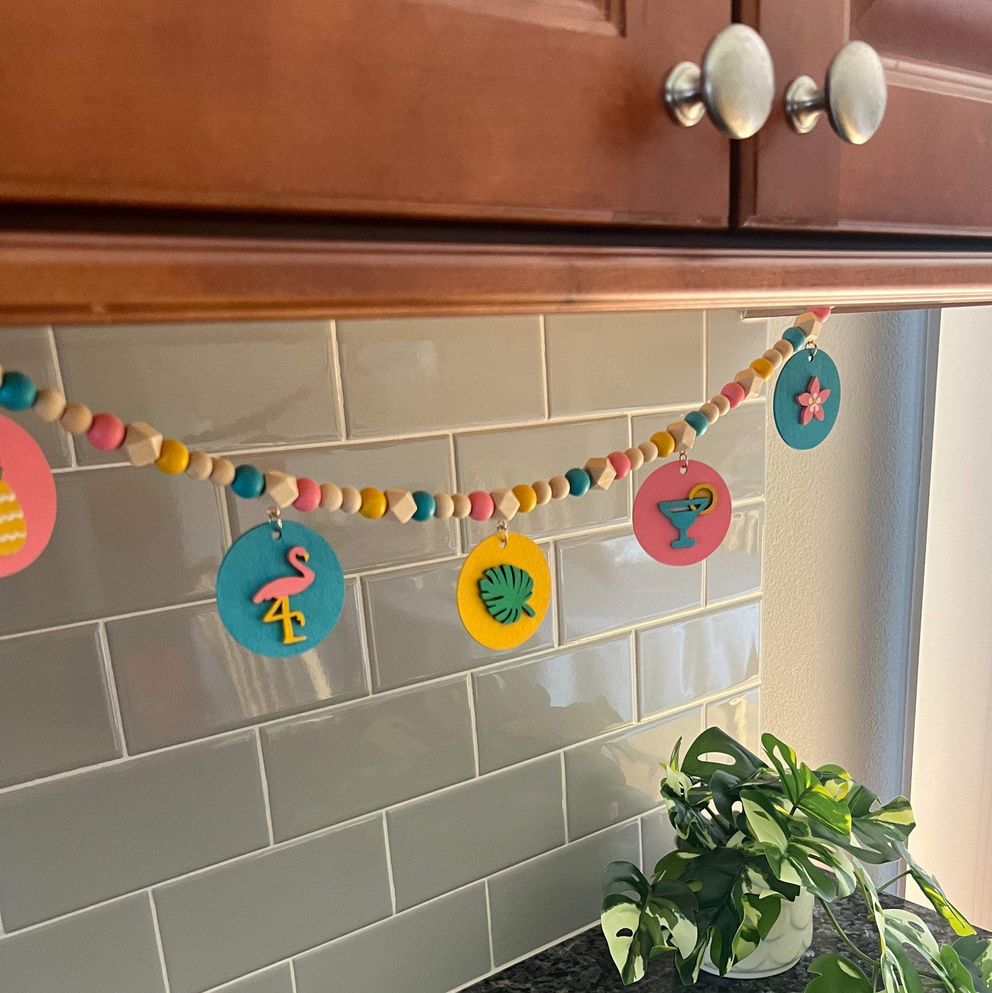 Tropical Little Vacay Mini Garland. Features wood shapes of a pineapple, flamingo, leaf, drink, and flower. Wood bead garland for summer, tropical theme decor or gift.