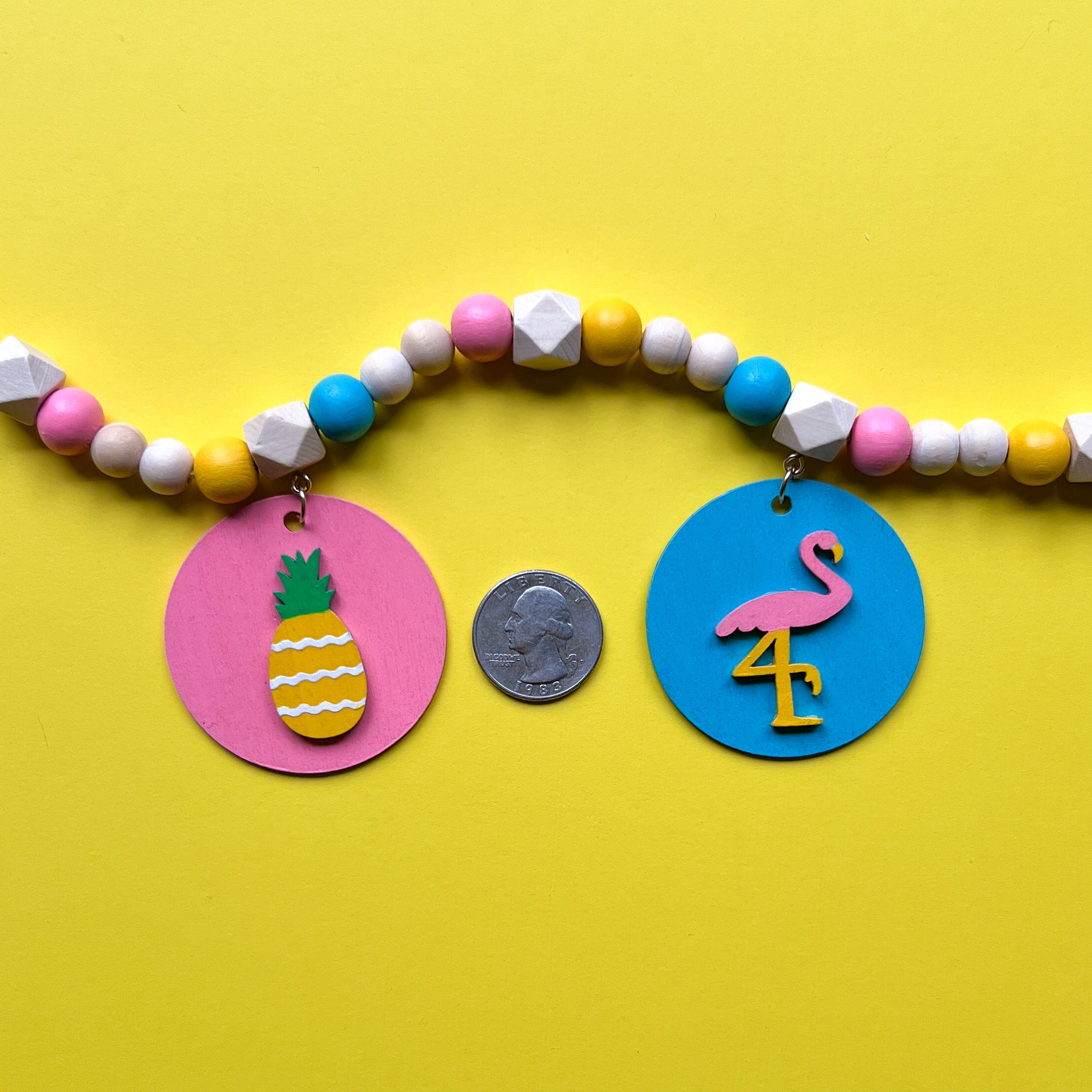 Tropical Little Vacay Mini Garland. Features wood shapes of a pineapple, flamingo, leaf, drink, and flower. Wood bead garland for summer, tropical theme decor or gift.
