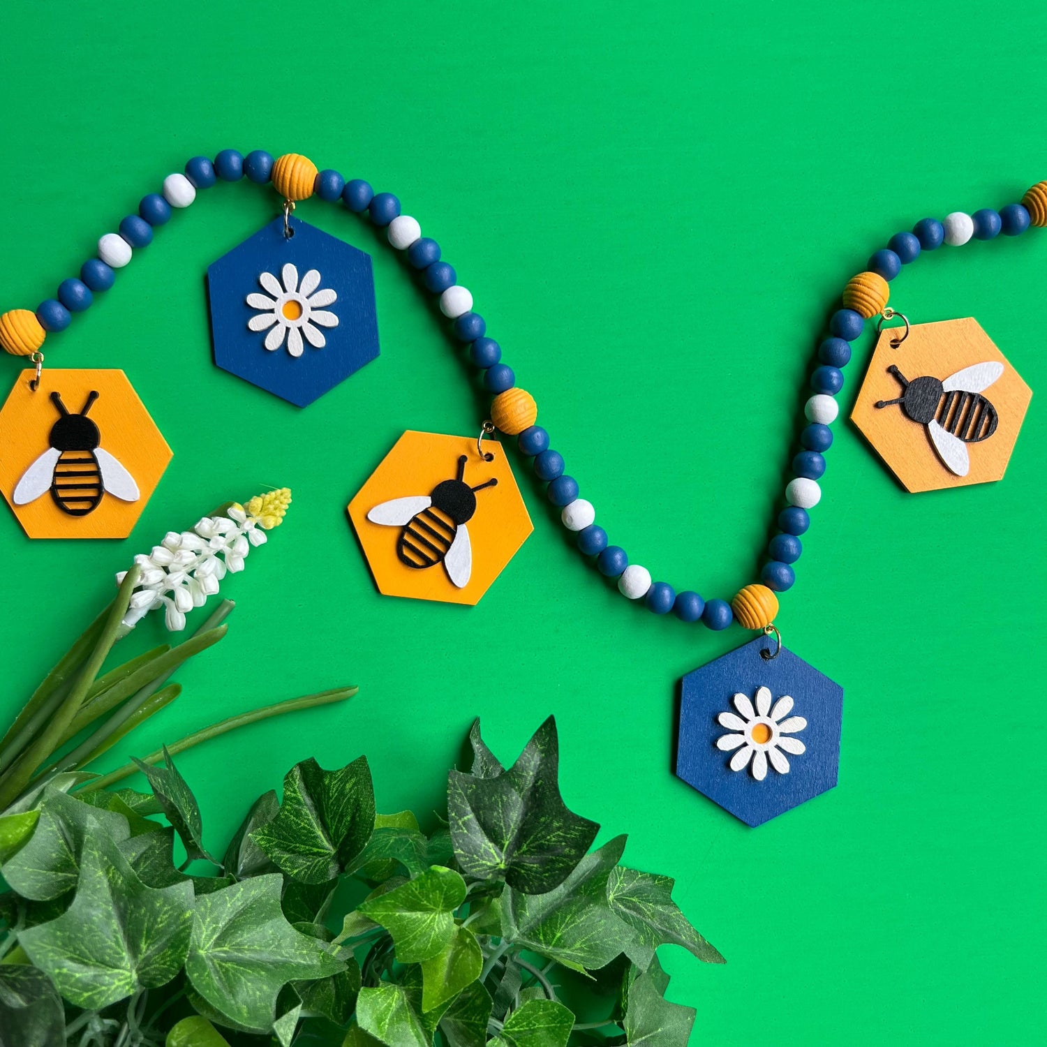Image of a small wood bead garland with circle elements that hang from square beads. These circles feature a cloud, flower, owl, toadstool, or bird. Garland is placed on a faux grass background.