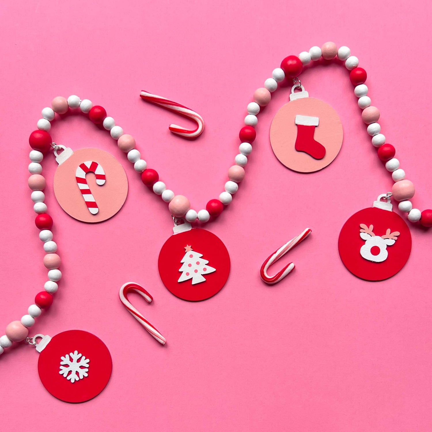 Holiday Cheer Handmade Garland. The garland features two decorated Christmas trees, two snowflakes, and one red ornament with a gingerbread man. Shapes hang from wood beads. Christmas holiday seasonal decoration or gift.