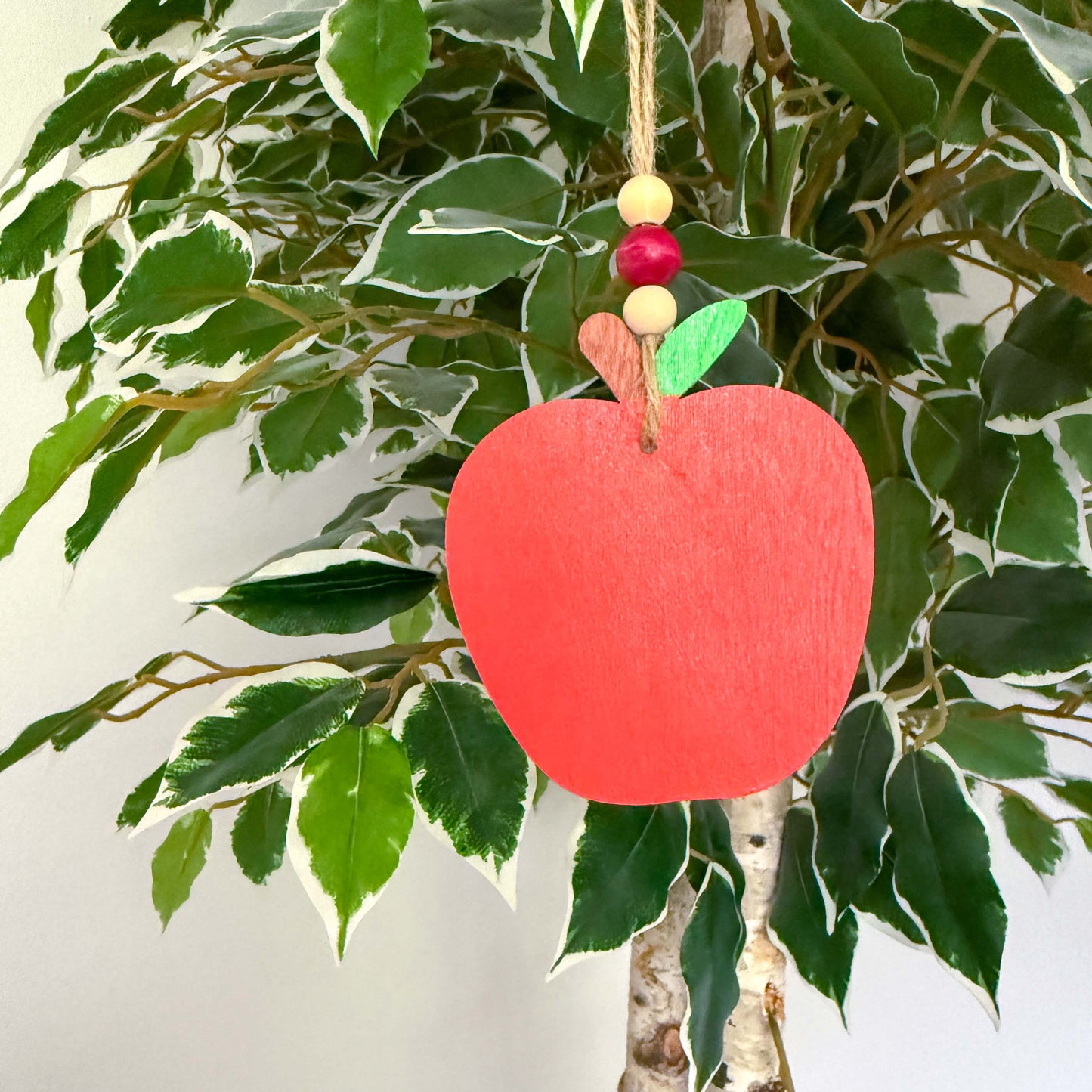 A wood apple ornament painted in bright red. Ornament hangs from jute twine and features three wood beads. 