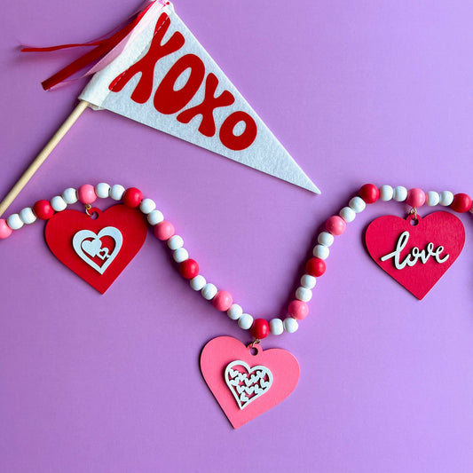 Be My Valentine Handmade Garland. Features red or pink wood hearts with smaller hearts or love text. Shapes hang from wood beads. Valentine's day decor or gfit.