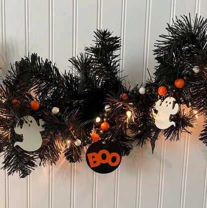 Boo to You Handmade Garland. The garland features seven Halloween themed shapes – jack-o-lanterns, ghosts, black cats, and a wood boo element in the center. Shapes hang from painted wood beads. Halloween fall seasonal decoration or gift.