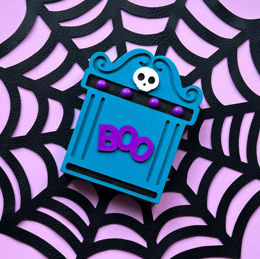 Bright Boo Tombstone Shelf Sitter. Features vibrant colors of blue and purple with a ‘boo’ wood cutout and a little skull. It's free standing, but has a keyhole cutout on the back so can hang on the wall. Halloween decor.