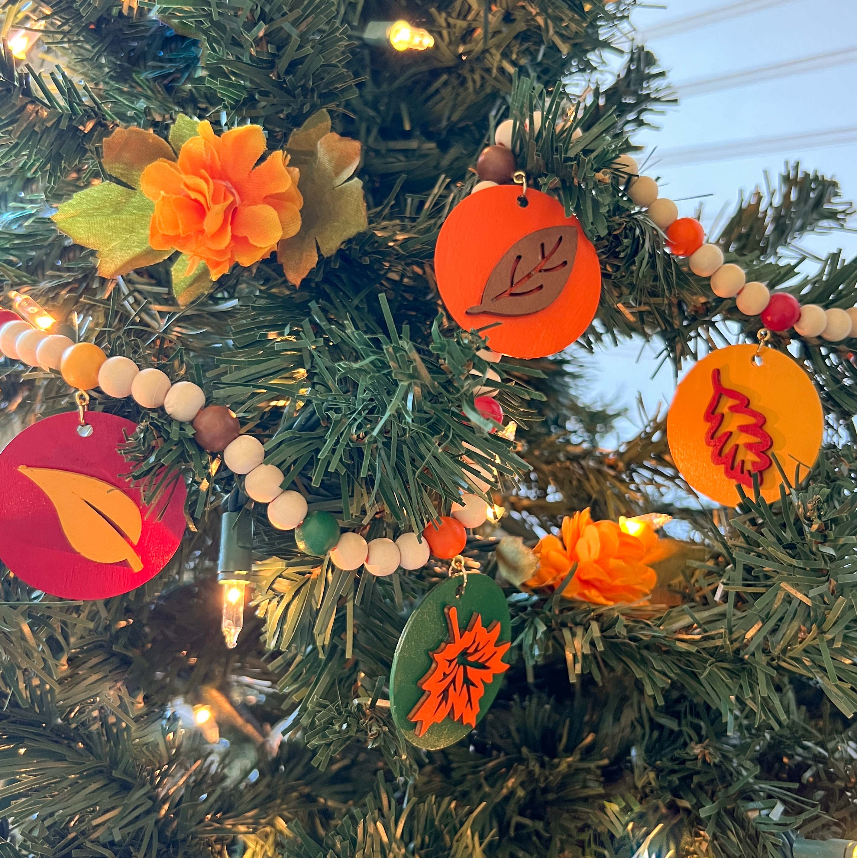 Image shows a wood bead garland with 2" wood circles that feature various colored fall leaves. Circles hang from painted beads with natural wood beads are interspersed. Beads are strung on 2mm orange macrame cord with 3" loops on each end.