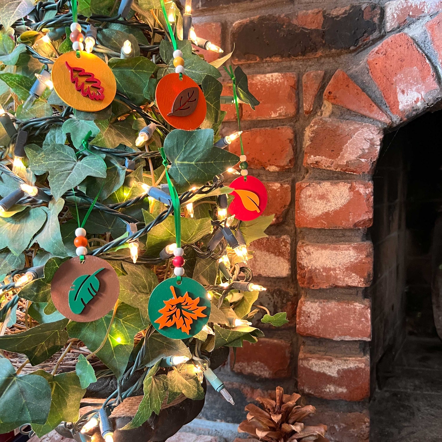 Fall themed ornaments featuring five 2-inch wood circles with wood leaves painted green, red, yellow, orange, or brown. Wood shapes hang from a green ribbon with three wood beads.