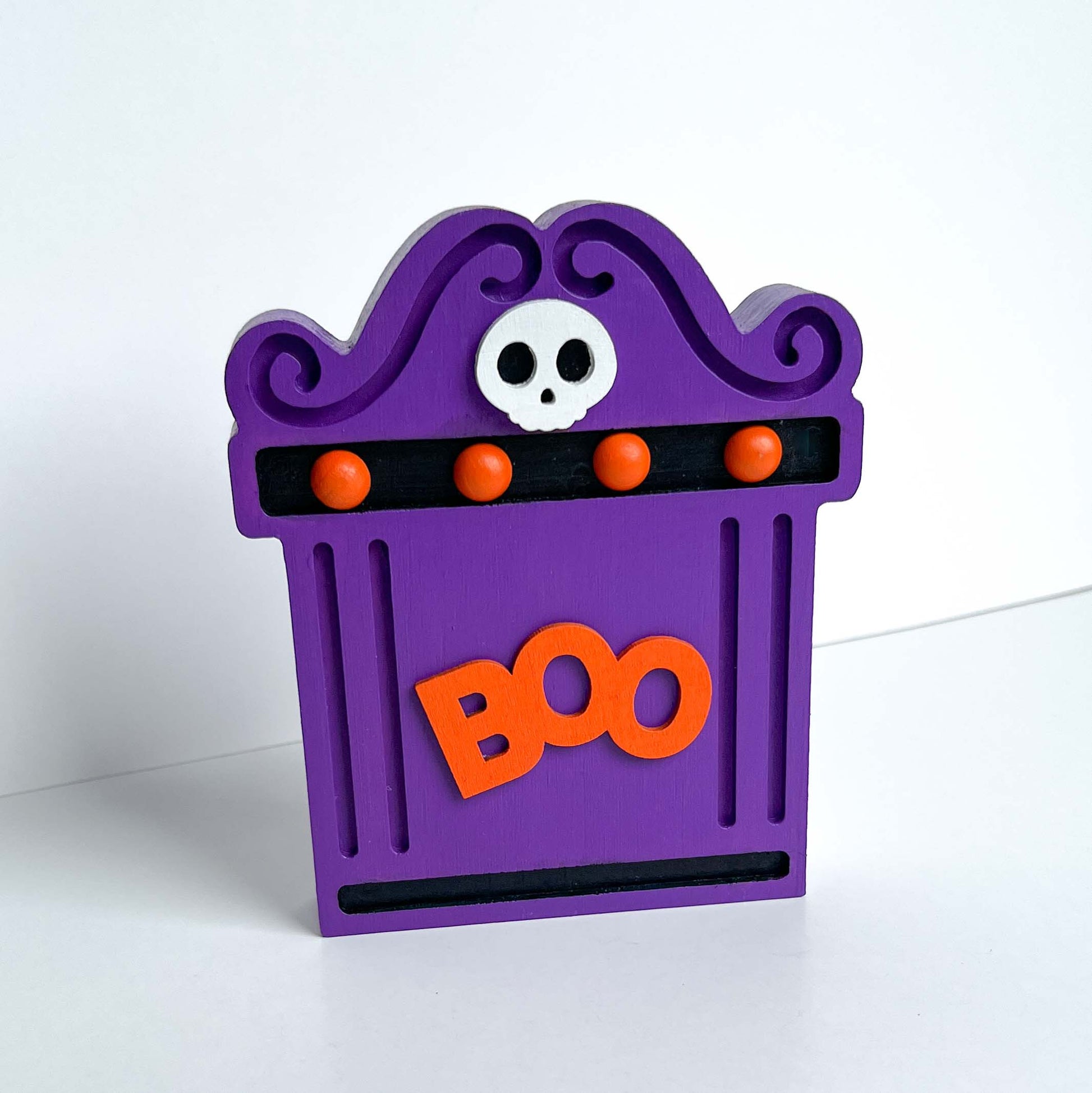 Bright Boo Tombstone Shelf Sitter. Features vibrant colors of purple and orange with a ‘boo’ wood cutout and a little skull. It is free standing, but has a keyhole cutout on the back so can hang on the wall. Halloween decor.