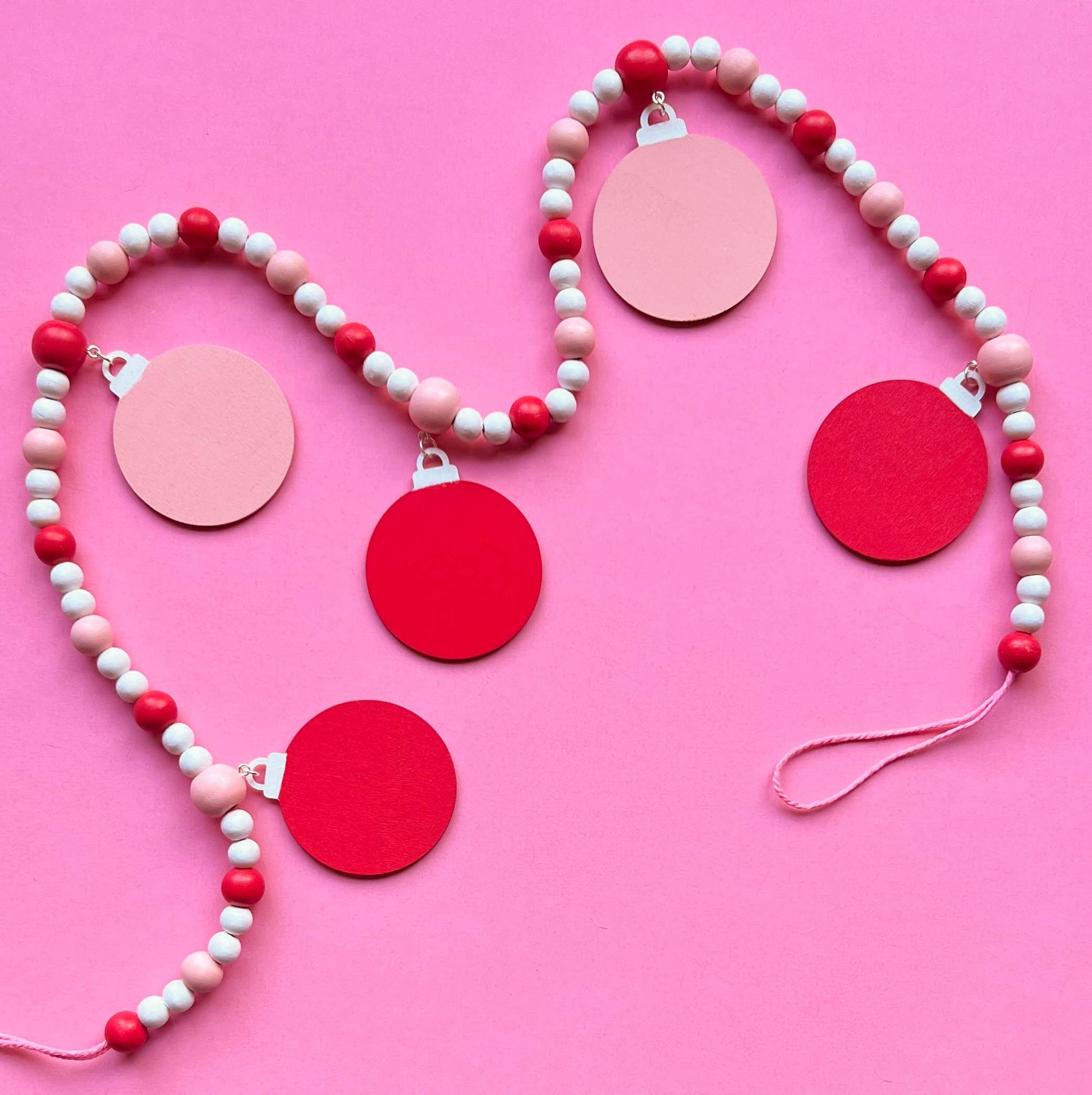 Candy cane colored holiday wood bead garland. Features five wood circles hanging from painted beads with holiday icons.