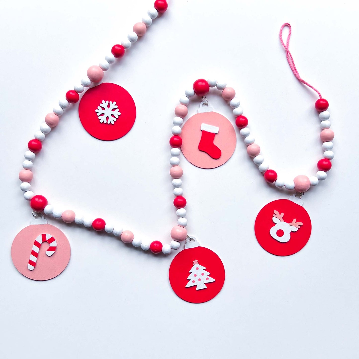 Candy cane colored holiday wood bead garland. Features five wood circles hanging from painted beads with holiday icons.