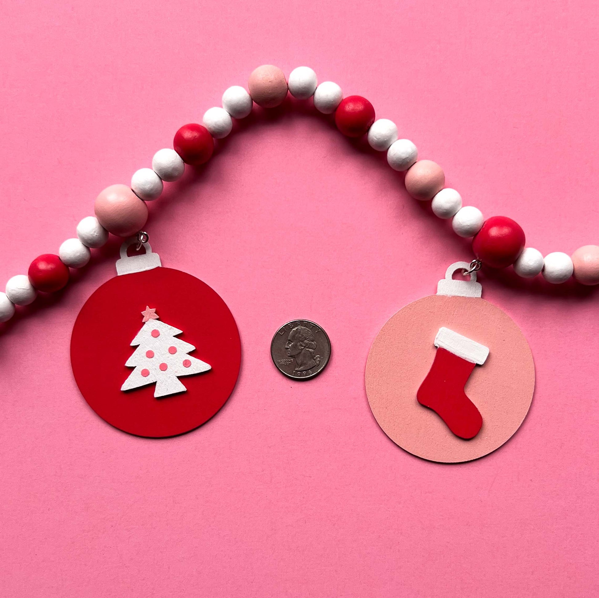 Candy cane colored holiday wood bead garland. Features five wood circles hanging from painted beads with holiday icons.