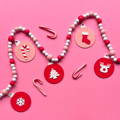 Candy cane colored holiday wood bead garland. Features five wood circles hanging from painted beads with holiday icons.