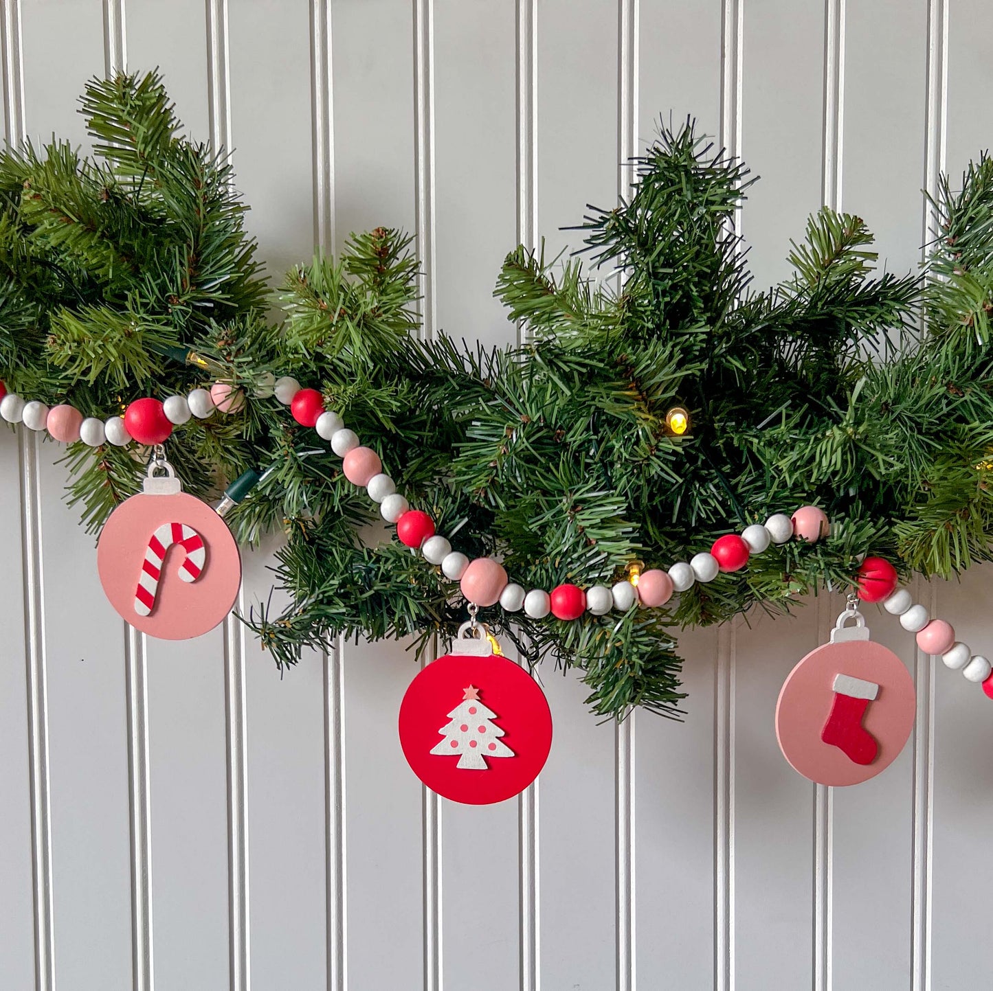 Candy cane colored holiday wood bead garland. Features five wood circles hanging from painted beads with holiday icons.