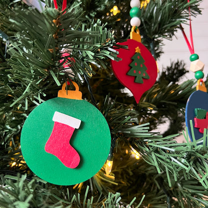 Image shows set of 3 flat wood handmade ornaments. Each ornament features a holiday themed wood shape: a decorated Christmas tree, a red stocking, or a truck bringing home the tree. Ornaments hang from ribbon and are decorated with three wood beads in matching colors.