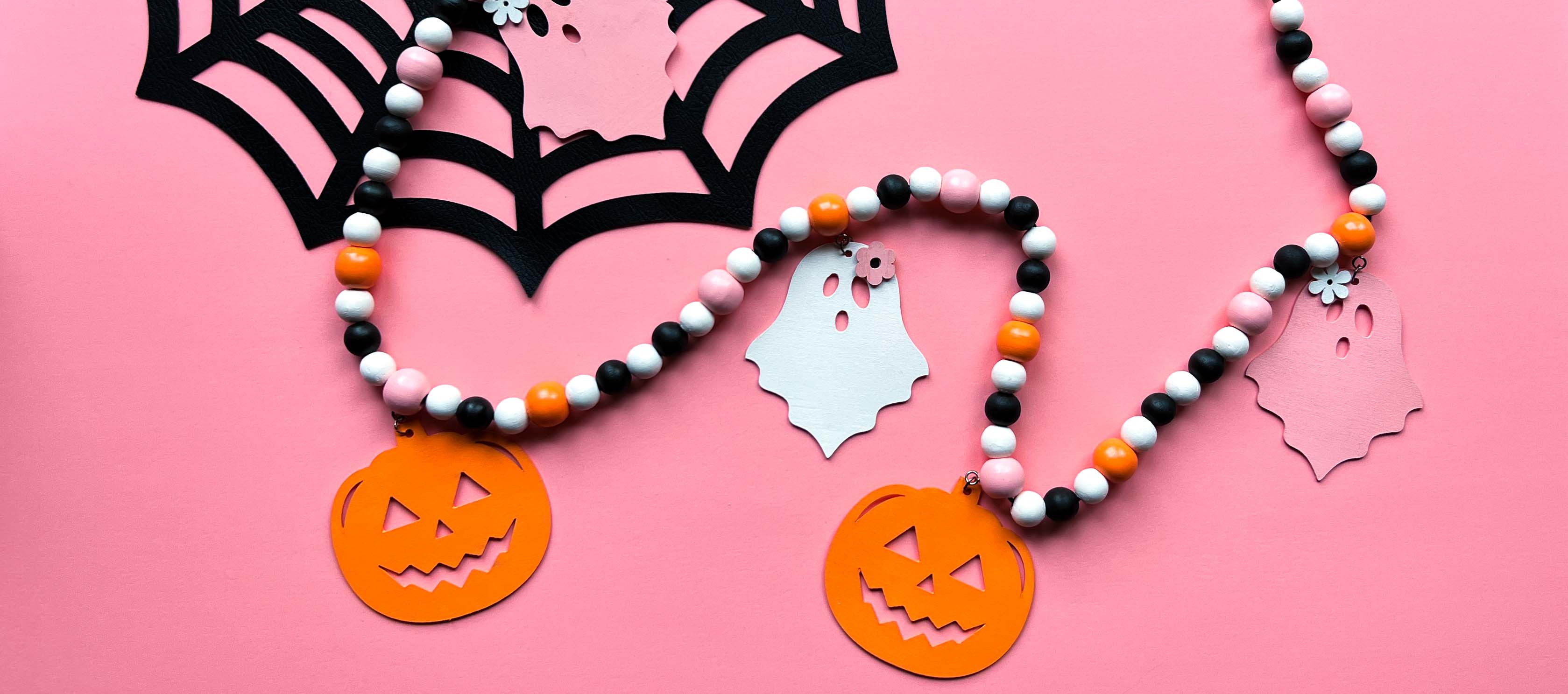 Halloween themed wood bead garland with three ghosts and two pumpkins hanging from beads. Black, white, light orange, pale pink beads and ghosts and pumpkins.