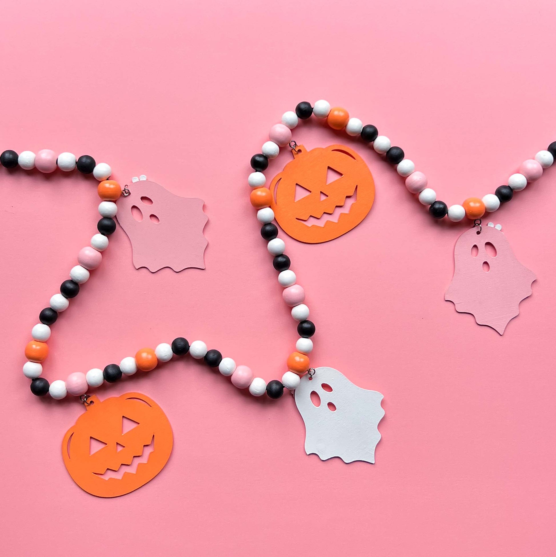 Halloween themed wood bead garland with three ghosts and two pumpkins hanging from beads. Black, white, light orange, pale pink beads and ghosts and pumpkins.