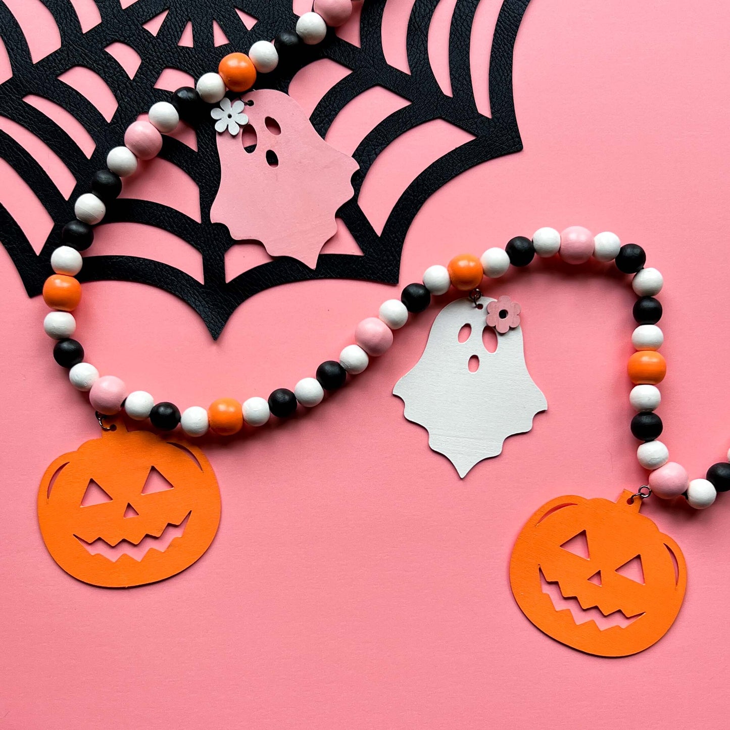 Halloween themed wood bead garland with three ghosts and two pumpkins hanging from beads. Black, white, light orange, pale pink beads and ghosts and pumpkins.