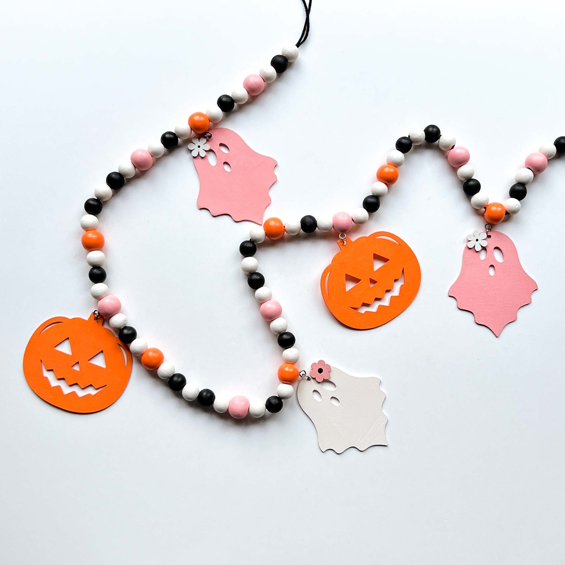 Halloween themed wood bead garland with three ghosts and two pumpkins hanging from beads. Black, white, light orange, pale pink beads and ghosts and pumpkins.