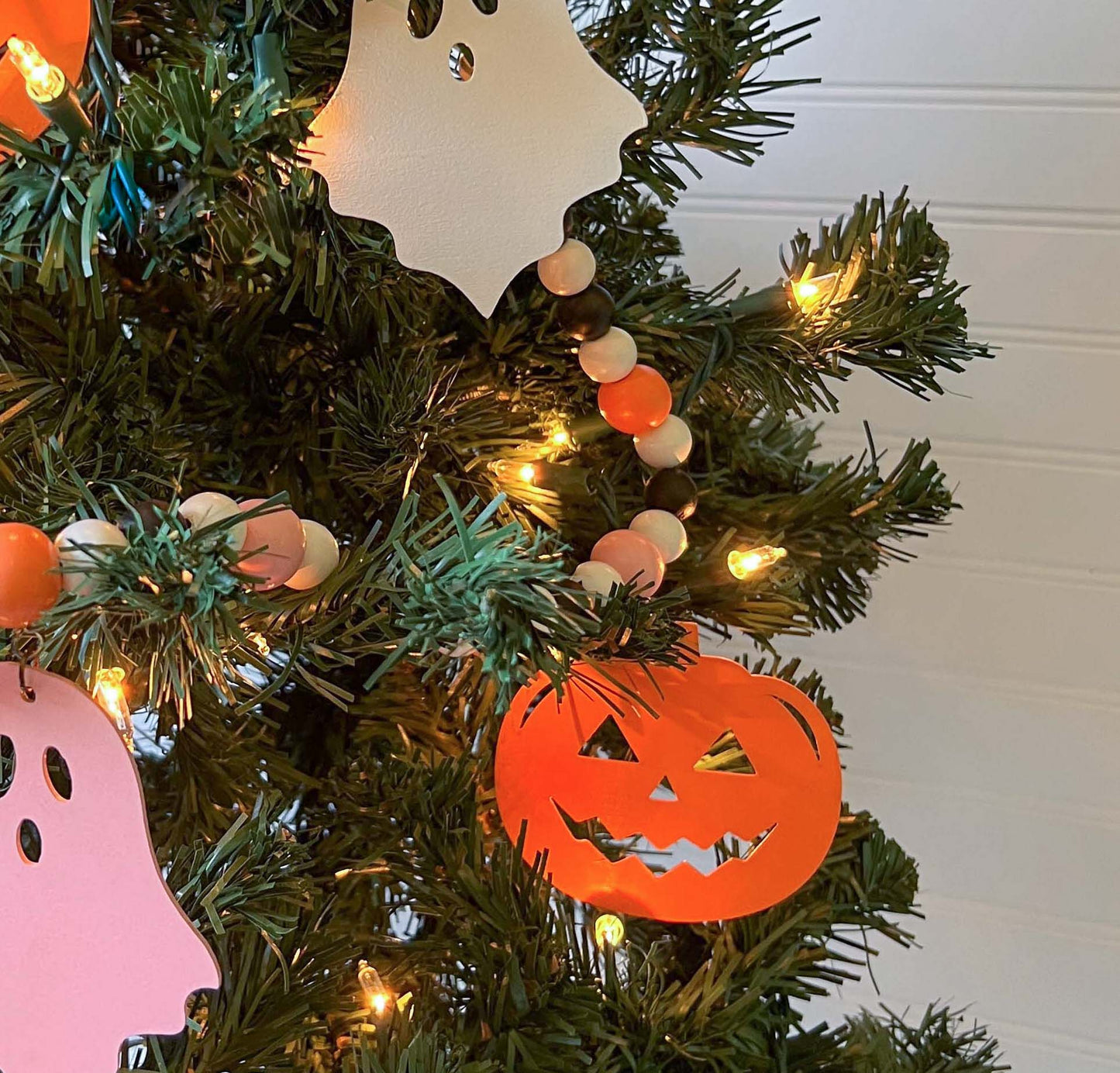 Halloween themed wood bead garland with three ghosts and two pumpkins hanging from beads. Black, white, light orange, pale pink beads and ghosts and pumpkins.