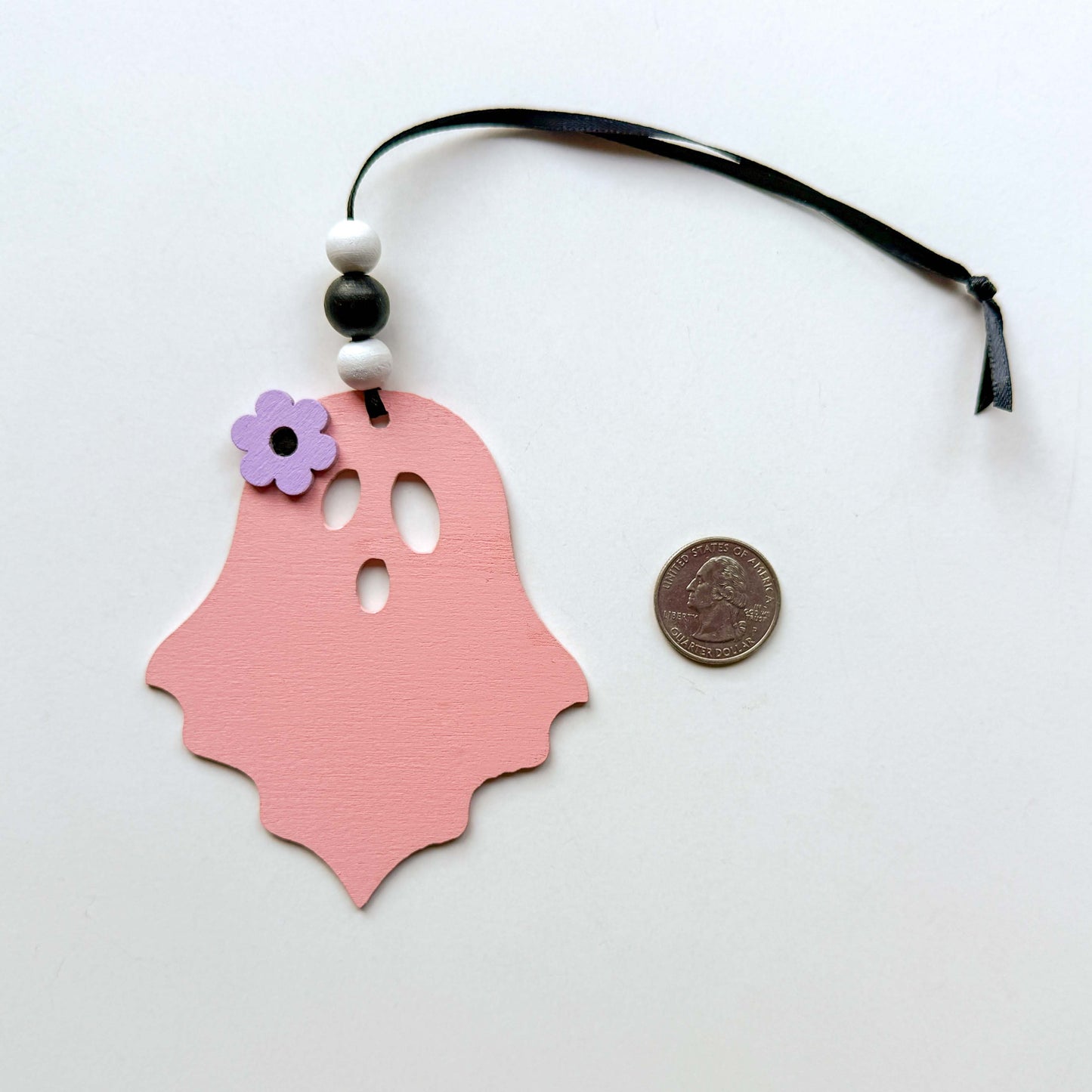 Wood ghost Halloween ornament in light pink, and featuring a flower accent. Ghost hangs from black ribbon; three wood beads in corresponding colors complete the ornament.