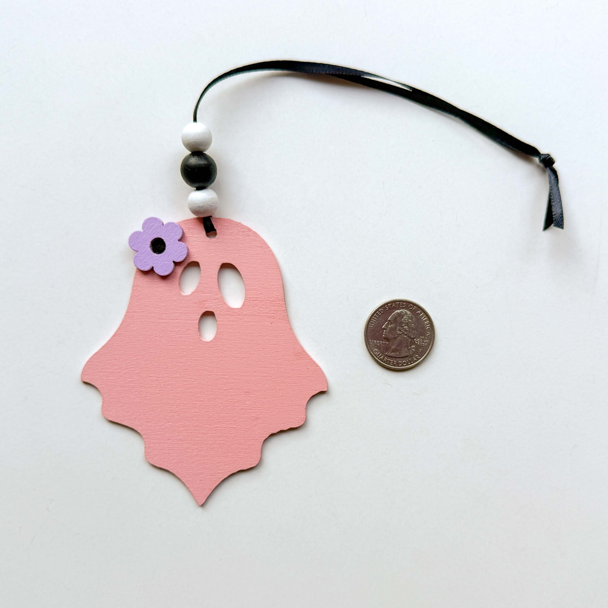 Wood ghost Halloween ornament in light pink, and featuring a flower accent. Ghost hangs from black ribbon; three wood beads in corresponding colors complete the ornament.