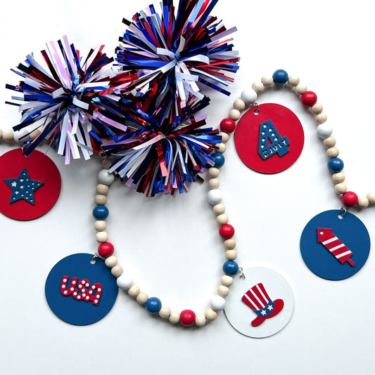 Happy 4th of July Handmade Garland. Features patriotic-themed shapes - a star, a "USA" and a 4th of July wood cutout, Uncle Sam's hat, and a firecracker. Summer red, white, blue decor and gifts.