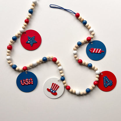 Happy 4th of July Handmade Garland. Features patriotic-themed shapes - a star, a "USA" and a 4th of July wood cutout, Uncle Sam's hat, and a firecracker. Summer red, white, blue decor and gifts.